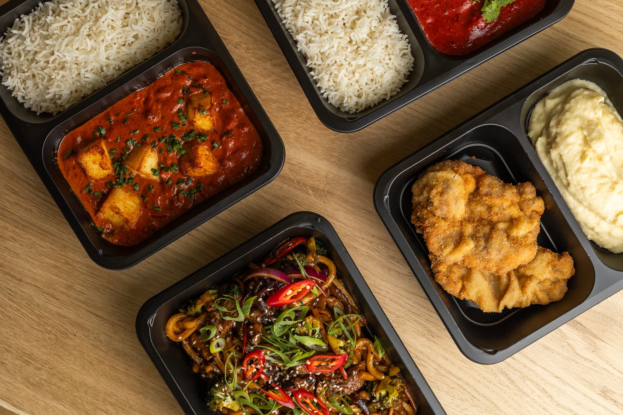 Hotová jídla Supper Lunch v krabičkách při pohledu shora — nudle se zeleninou a chilli, kari s rýží a smažený řízek s bramborovou kaší